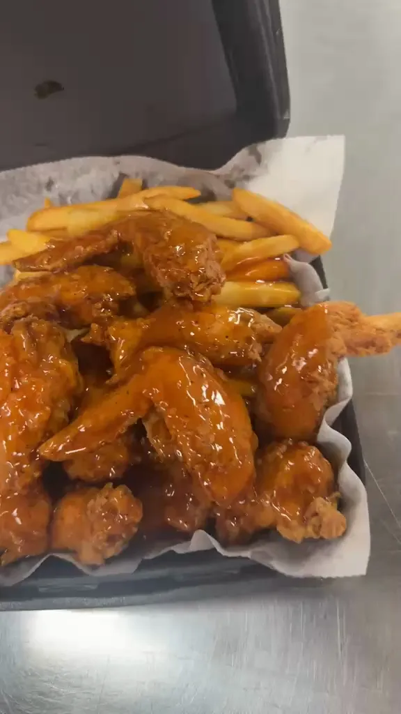 Whole wings glazed in glossy orange sauce piled over fries in a paper-lined basket