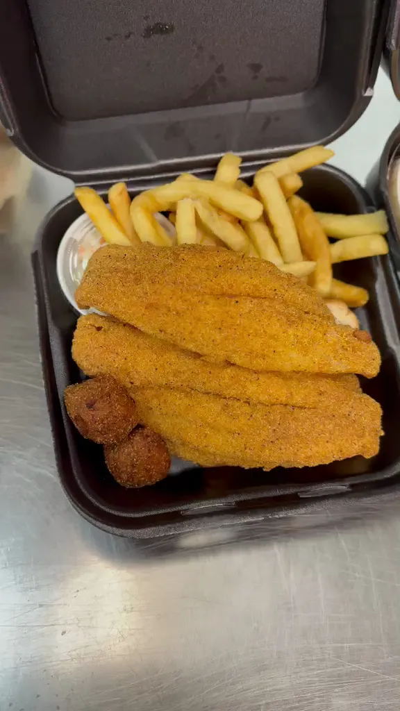 A takeout box of cornmeal-breaded catfish fillets with fries, hush puppies and coleslaw