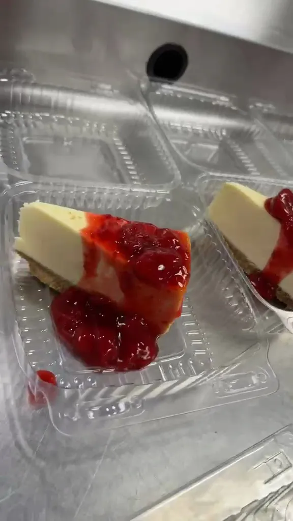 A slice of cheesecake with glossy strawberry topping in a clear dessert container