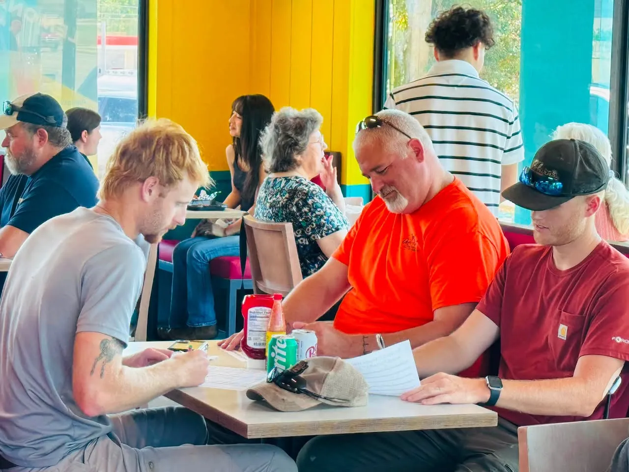 Guests eating at tables in the Sharks De Queen dining room, with yellow walls and turquoise booths