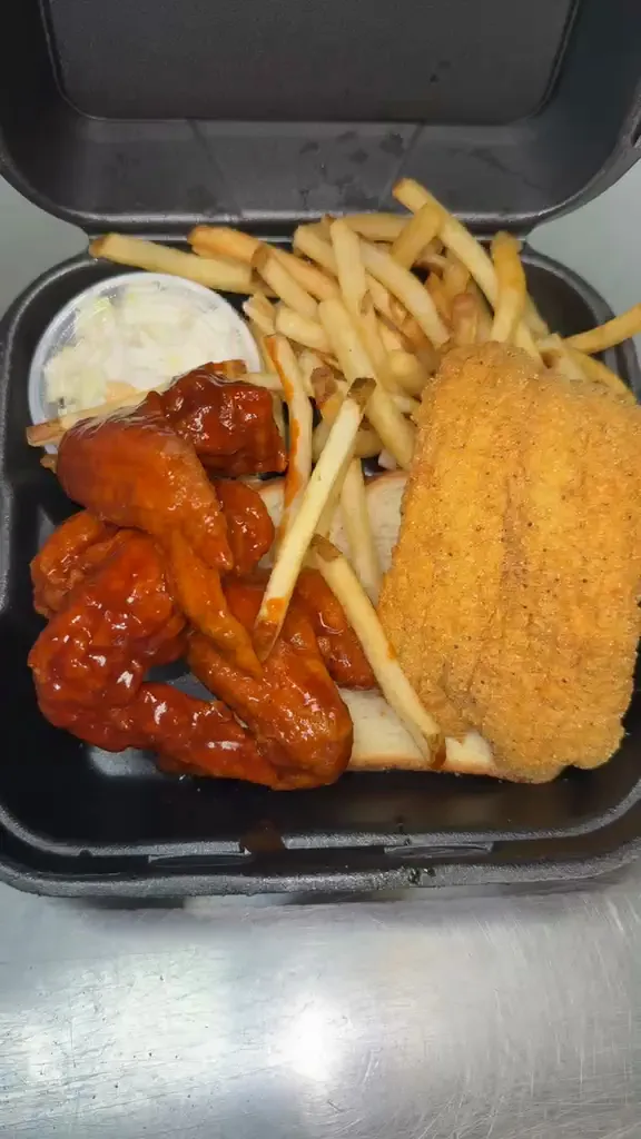Breaded fish beside dark-glazed wings with fries and a cup of coleslaw
