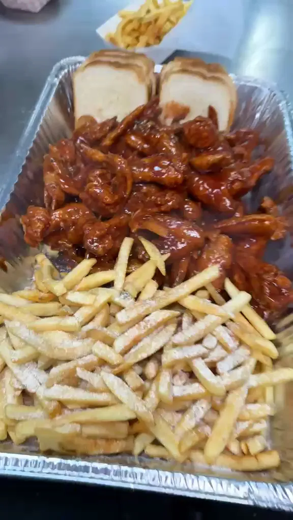A large foil tray of glazed whole wings with seasoned fries and sliced white bread