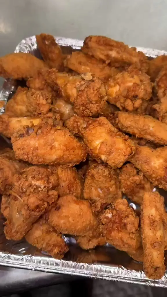 A foil catering tray piled with fried whole chicken wings